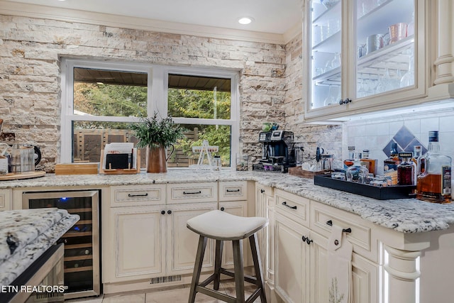 bar with cream cabinetry, wine cooler, decorative backsplash, and light stone counters