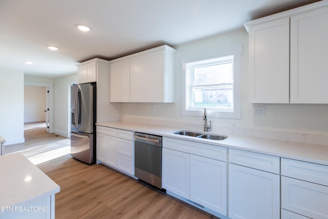 kitchen featuring sink, white cabinets, appliances with stainless steel finishes, and light wood-type flooring