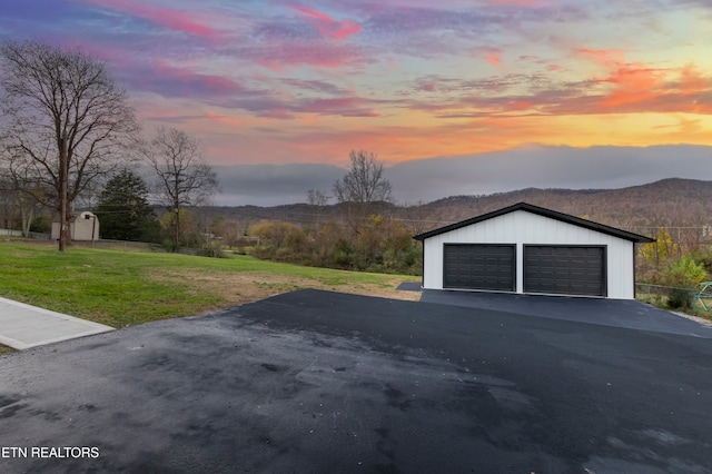 garage at dusk with a mountain view and a lawn