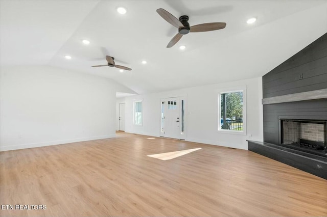 unfurnished living room with ceiling fan, vaulted ceiling, a large fireplace, and light hardwood / wood-style floors