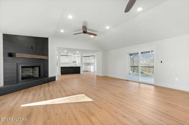 unfurnished living room with vaulted ceiling, a large fireplace, and light hardwood / wood-style flooring