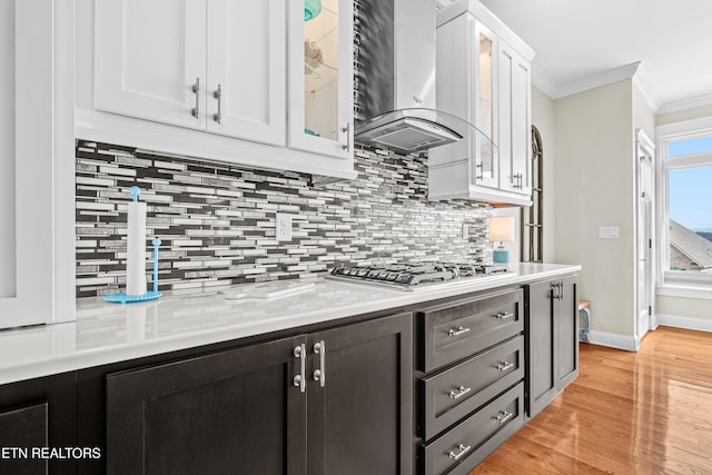 kitchen with light hardwood / wood-style floors, white cabinetry, ornamental molding, stainless steel gas stovetop, and wall chimney range hood