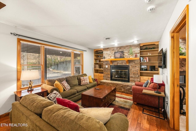 living room with a stone fireplace, built in features, wood-type flooring, and a textured ceiling