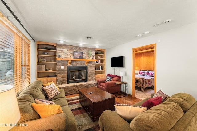 living room with built in shelves, a stone fireplace, a textured ceiling, and light hardwood / wood-style floors