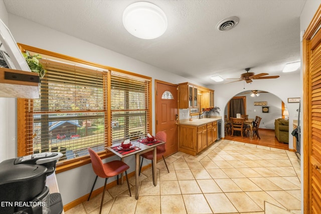 kitchen featuring light tile patterned flooring, tile countertops, sink, ceiling fan, and a textured ceiling