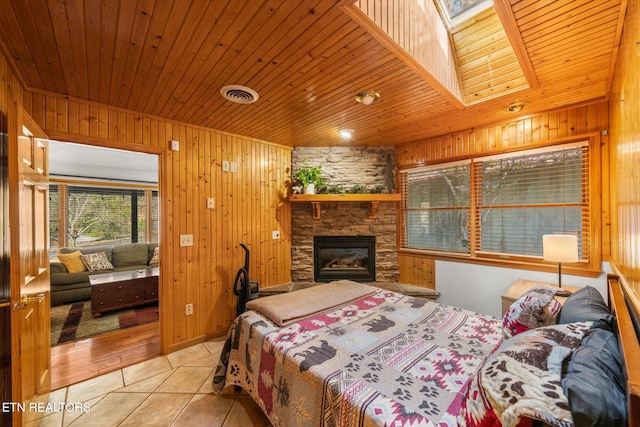 bedroom with a stone fireplace, wood walls, wooden ceiling, and light tile patterned floors