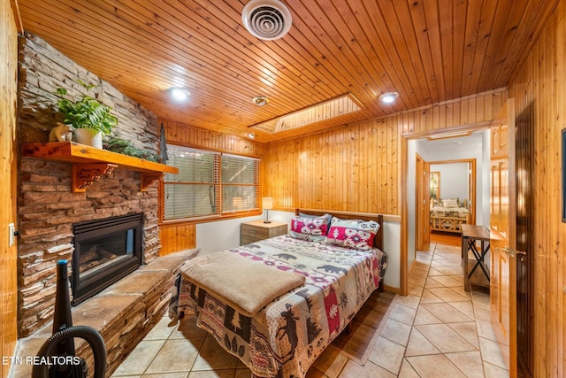 tiled bedroom featuring wooden ceiling, a stone fireplace, wood walls, and a skylight