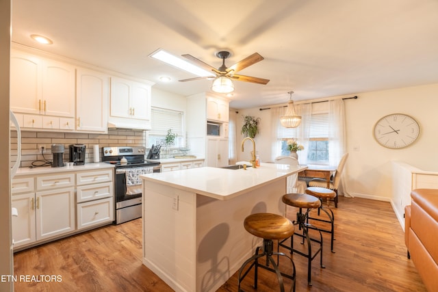 kitchen featuring stainless steel electric range, a kitchen island with sink, white cabinets, and pendant lighting