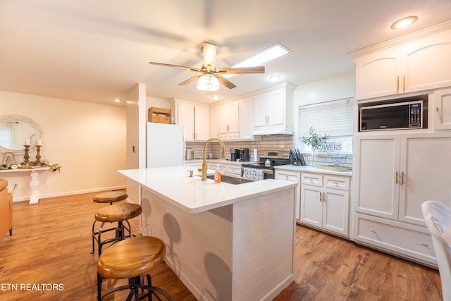 kitchen featuring electric stove, sink, built in microwave, white fridge, and white cabinetry