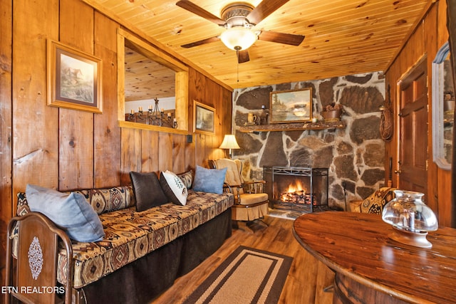 living room with a stone fireplace, wood walls, hardwood / wood-style flooring, ceiling fan, and wooden ceiling