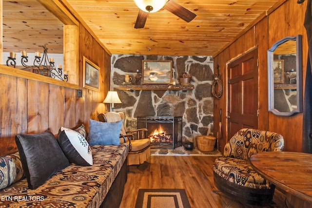 living room featuring dark hardwood / wood-style floors, a stone fireplace, wooden walls, and wood ceiling