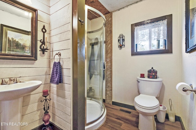 bathroom featuring wooden walls, toilet, a shower with door, and hardwood / wood-style floors