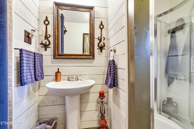 bathroom with bath / shower combo with glass door and wood walls