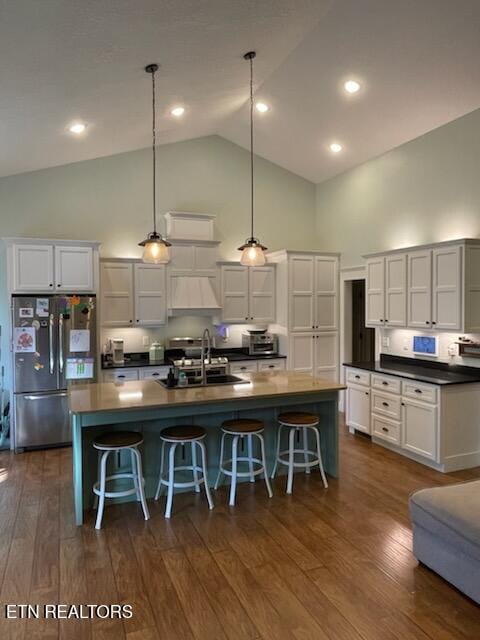 kitchen featuring stainless steel refrigerator, sink, dark wood-type flooring, hanging light fixtures, and an island with sink