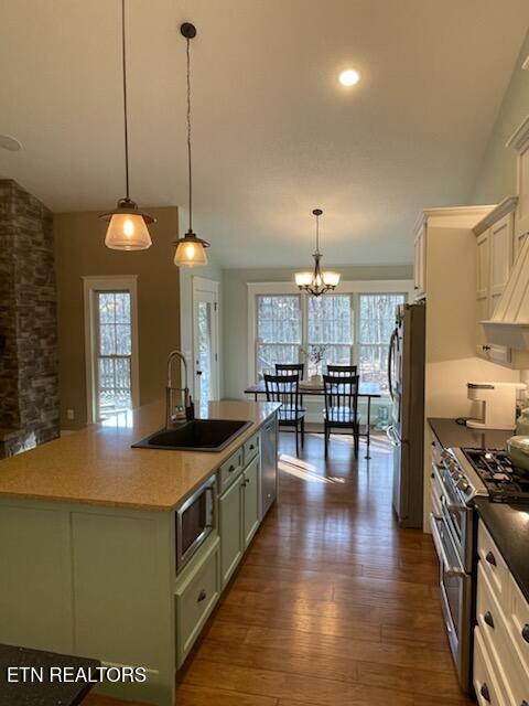 kitchen featuring sink, hanging light fixtures, green cabinets, a center island with sink, and appliances with stainless steel finishes