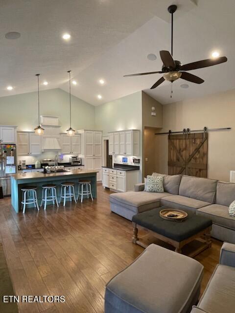 living room featuring a barn door, hardwood / wood-style flooring, high vaulted ceiling, and ceiling fan