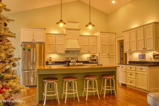 kitchen with a kitchen breakfast bar, a center island with sink, hardwood / wood-style floors, stainless steel refrigerator, and hanging light fixtures