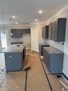 kitchen featuring sink, crown molding, a kitchen island with sink, backsplash, and decorative light fixtures