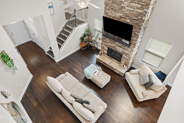 living room featuring a fireplace, a towering ceiling, dark hardwood / wood-style floors, and ceiling fan