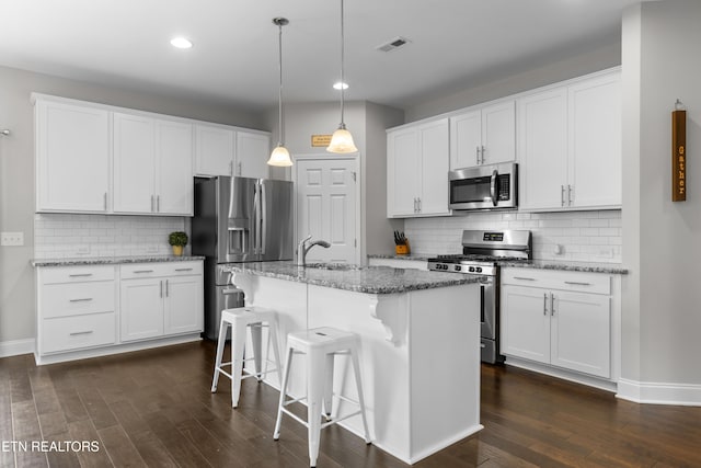 kitchen with white cabinets, appliances with stainless steel finishes, decorative light fixtures, and a kitchen island with sink