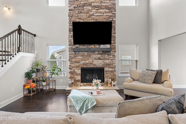 living room with a high ceiling, a stone fireplace, and dark wood-type flooring