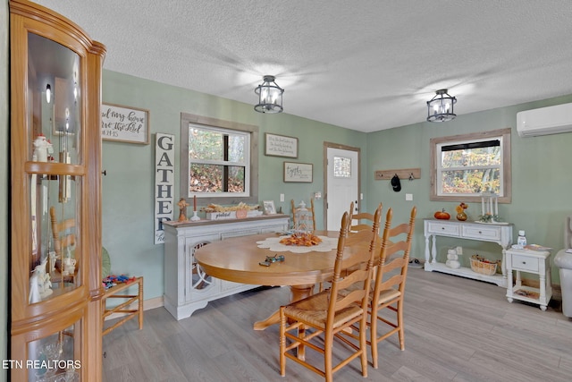 dining space featuring a textured ceiling, light wood-type flooring, and an AC wall unit