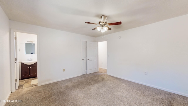 unfurnished bedroom featuring ensuite bathroom, ceiling fan, sink, and light colored carpet