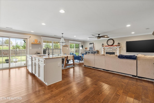 kitchen featuring sink, decorative light fixtures, a center island with sink, white cabinets, and light hardwood / wood-style floors