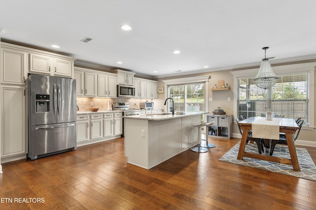 kitchen with pendant lighting, dark wood-type flooring, a center island with sink, crown molding, and stainless steel appliances