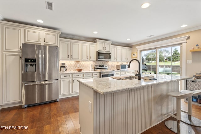 kitchen featuring light stone countertops, appliances with stainless steel finishes, a center island with sink, and dark wood-type flooring