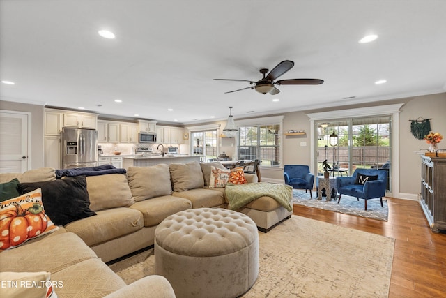 living room featuring light hardwood / wood-style floors, ceiling fan, ornamental molding, and sink