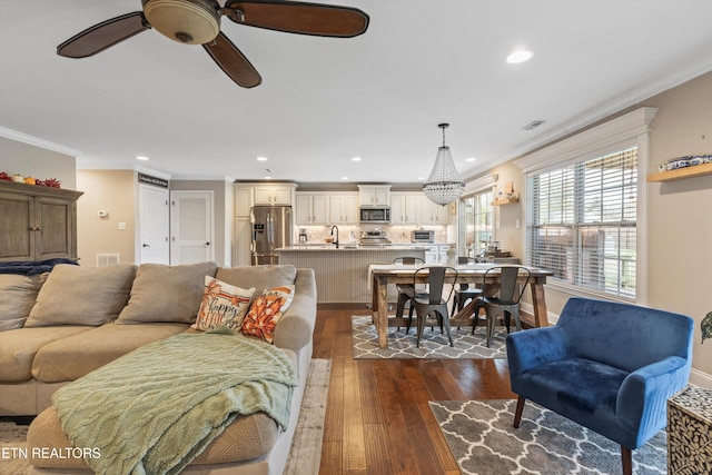 living room featuring ceiling fan with notable chandelier, sink, ornamental molding, and dark wood-type flooring