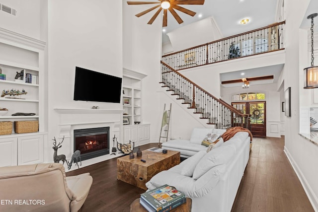 living room featuring ceiling fan, a high ceiling, dark hardwood / wood-style floors, and built in features