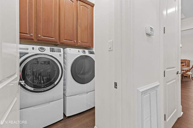 clothes washing area with dark wood-type flooring, cabinets, and washing machine and dryer