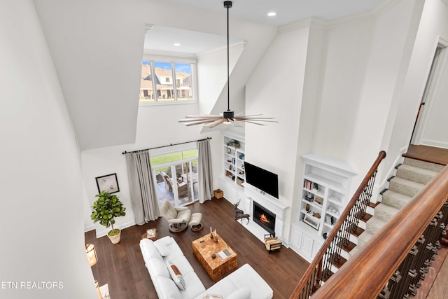 living room with dark wood-type flooring, ceiling fan, and crown molding