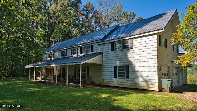 back of house featuring a garage, covered porch, and a yard