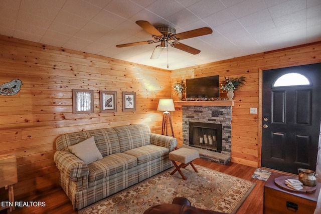 living room with a fireplace, wooden walls, hardwood / wood-style flooring, and ceiling fan