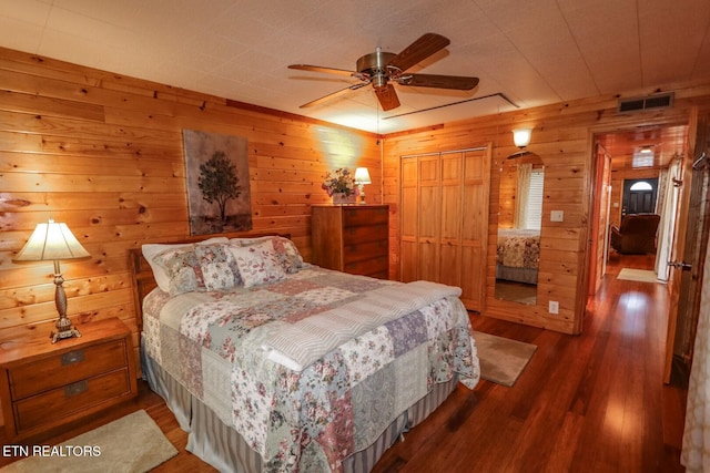 bedroom featuring dark wood-type flooring, ceiling fan, wooden walls, and a closet