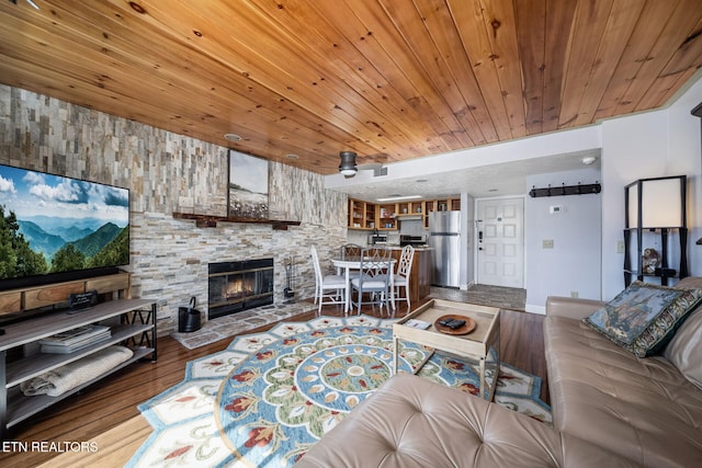 living room featuring ceiling fan, hardwood / wood-style flooring, a stone fireplace, and wood ceiling