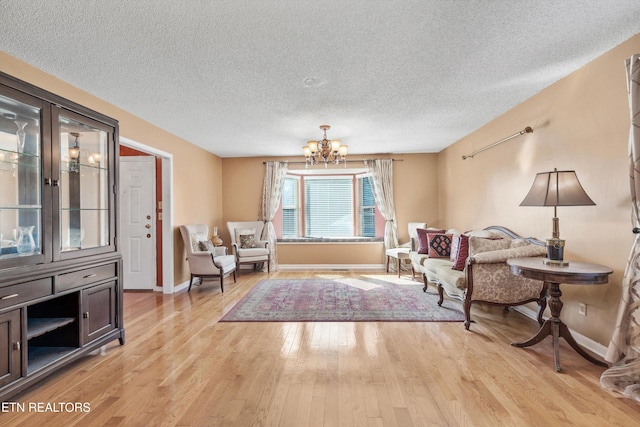 living area with an inviting chandelier, a textured ceiling, and light hardwood / wood-style flooring