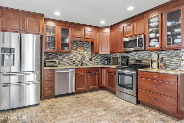 kitchen featuring backsplash, light stone countertops, sink, and appliances with stainless steel finishes