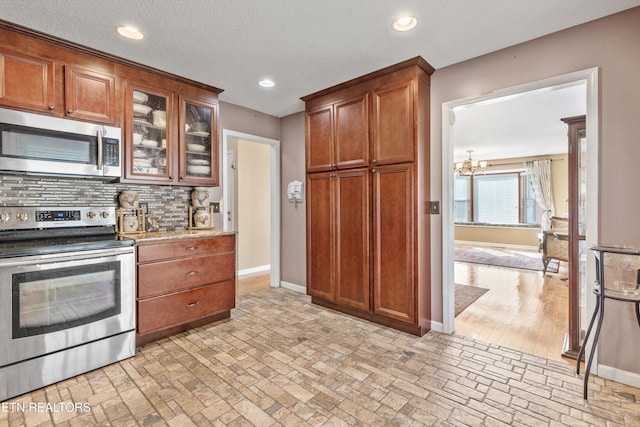 kitchen with light stone countertops, appliances with stainless steel finishes, backsplash, a textured ceiling, and an inviting chandelier