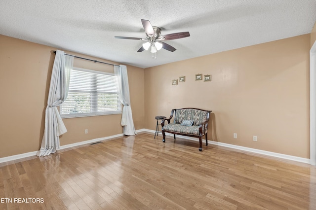 living area featuring a textured ceiling, light hardwood / wood-style floors, and ceiling fan