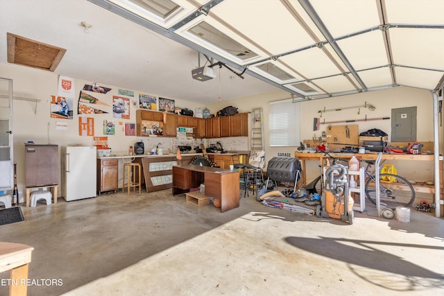 garage featuring a workshop area, white fridge, a garage door opener, and electric panel