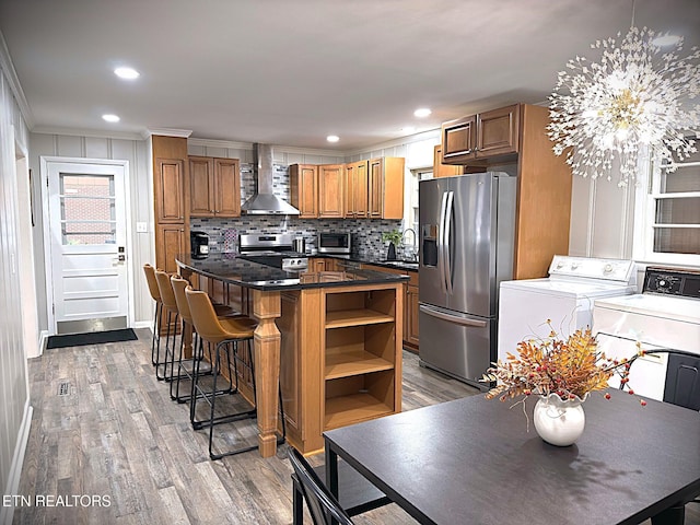 kitchen with appliances with stainless steel finishes, light wood-type flooring, wall chimney exhaust hood, pendant lighting, and washing machine and clothes dryer