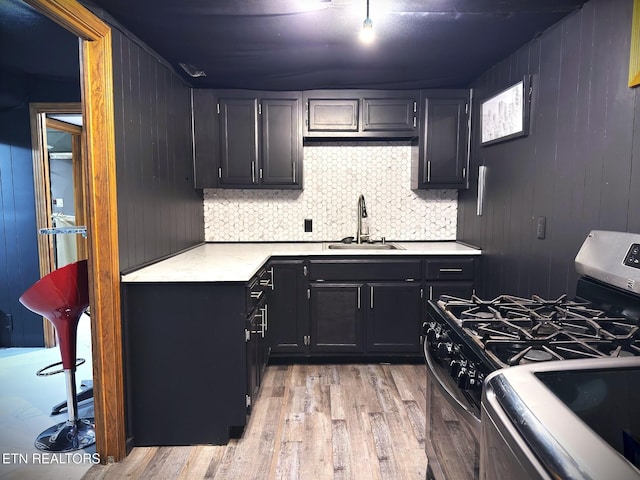 kitchen with backsplash, sink, wooden walls, light hardwood / wood-style floors, and range with gas cooktop