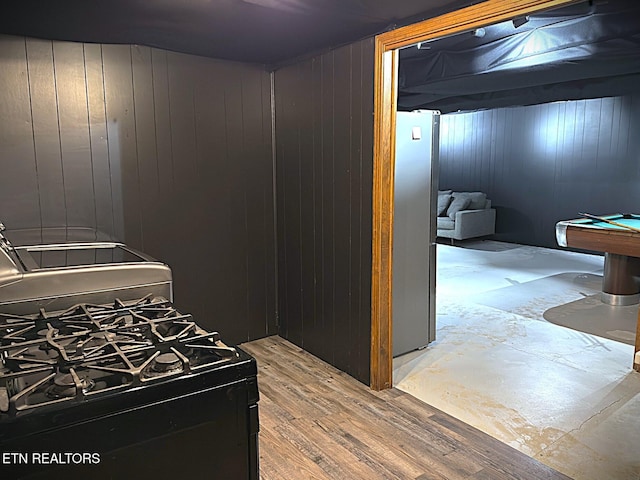 kitchen with stainless steel refrigerator, hardwood / wood-style floors, black range with gas cooktop, wooden walls, and pool table