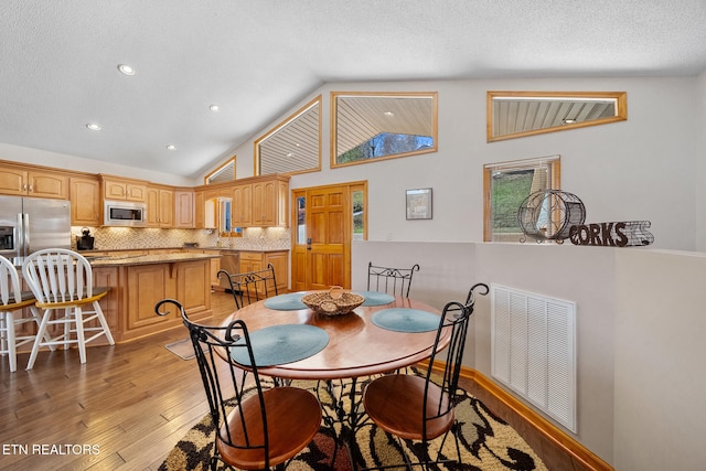 dining room with light wood-type flooring, a textured ceiling, and high vaulted ceiling