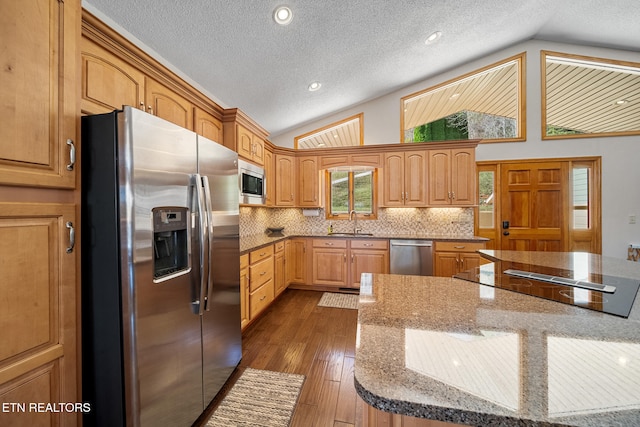 kitchen with sink, appliances with stainless steel finishes, light stone countertops, dark wood-type flooring, and vaulted ceiling