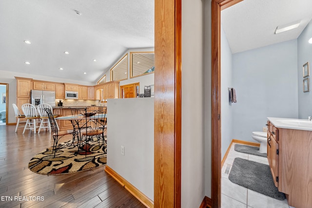 kitchen featuring appliances with stainless steel finishes, light brown cabinetry, vaulted ceiling, light hardwood / wood-style floors, and a breakfast bar area